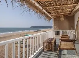 Balcony with chairs and thatched roof overlooking beach.