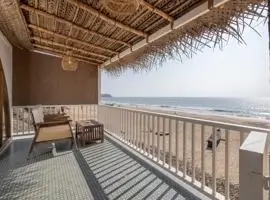 A beachfront balcony with cozy chairs and a thatched roof, offering a perfect spot to relax and enjoy the view.